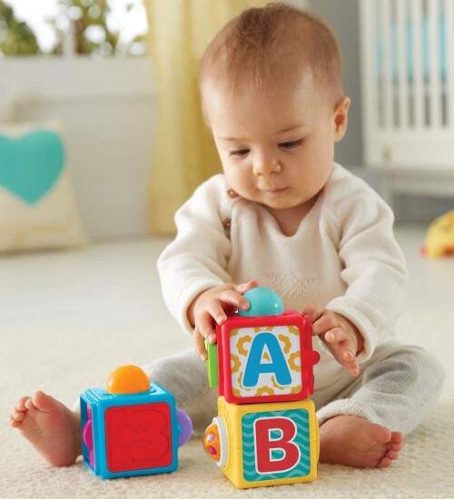 El bebe de 9 meses sentado con 3 cubos de actividades 